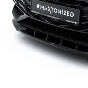 Close-up of a black car's front end with a glossy grille and a license plate reading '#MAXTONIZED'.