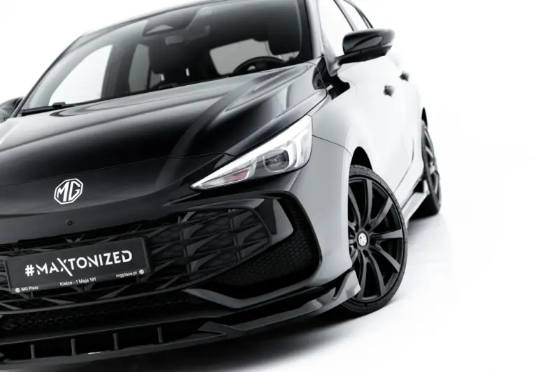 Close-up of a sleek black MG car front with prominent MG badge and a bold #MAXTONIZED license area, angled view showing headlight and grille.