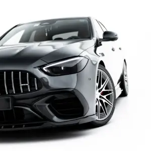 Front-left close-up of a dark gray Mercedes-Benz AMG, showing the vertical slat grille, emblem, headlight, and glossy hood against a white background