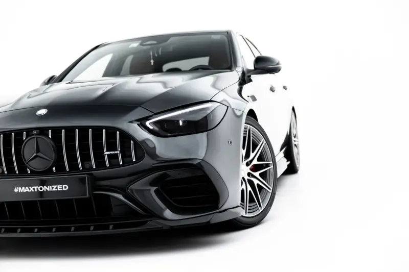 Front-left close-up of a dark gray Mercedes-Benz AMG, showing the vertical slat grille, emblem, headlight, and glossy hood against a white background