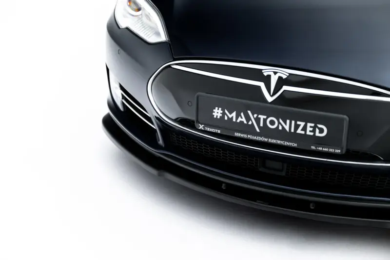 Front-close view of a black Tesla, showing the emblem and a plate reading #MAXTONIZED.