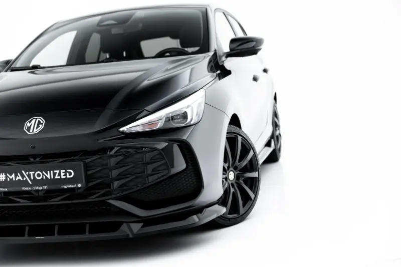 Front-left view of a sleek black MG car, highlighting the emblem, grille, and sharp headlight against a white background with glossy finish.