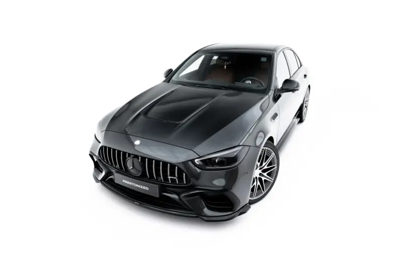 Front three-quarter view of a dark gray Mercedes-Benz AMG car with prominent grille and large alloy wheels against a white studio background, angled from above.