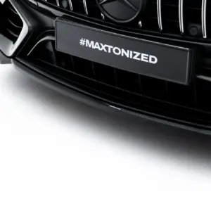 Close-up of a black car grille with #MAXTONIZED branding on the license plate area and AMG badge visible