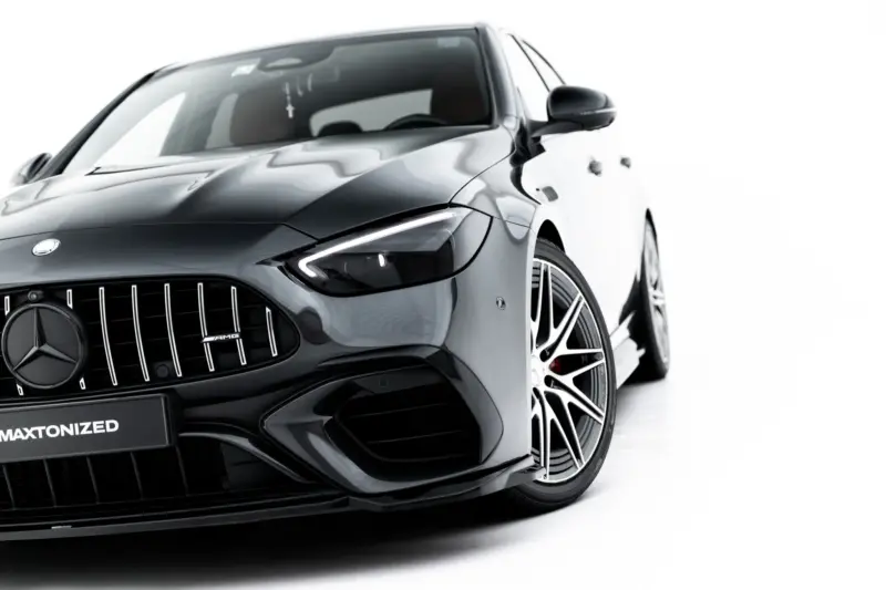 Front-left view of a sleek dark-gray Mercedes-Benz car, highlighting the distinctive grille and sharp headlight.