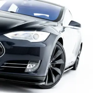 Close-up of a glossy black car front, featuring the headlight, bumper, and wheel in view.