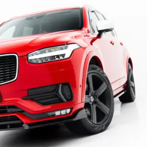 Red Volvo SUV shown from a low front-left angle, featuring the grille, headlight, and wheel against a white backdrop.
