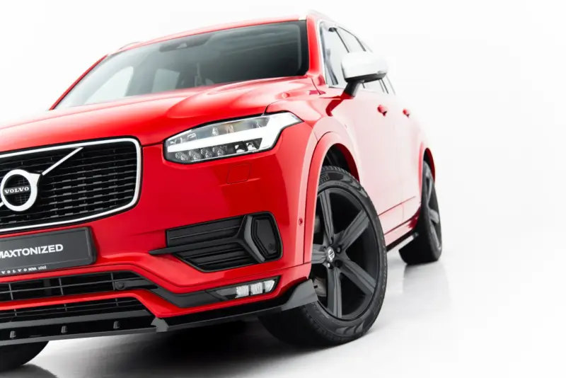 Red Volvo SUV shown from a low front-left angle, featuring the grille, headlight, and wheel against a white backdrop.
