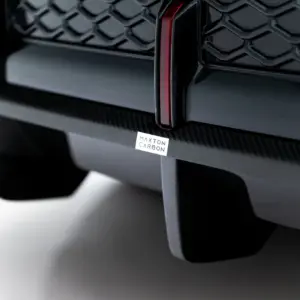 Close-up of a carbon fiber car part with a small Maxton Carbon badge.