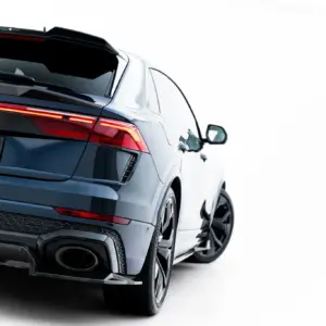Rear three-quarter view of a dark blue Audi SUV with illuminated taillights and a carbon-fiber spoiler, seen from the left side.