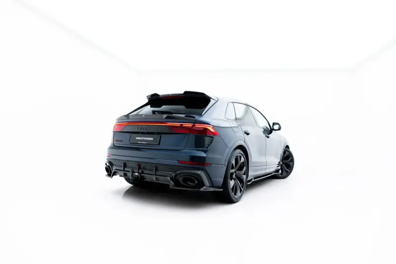 Rear three-quarter view of a blue Audi SUV in a white studio setting, with lit taillights visible on the back.