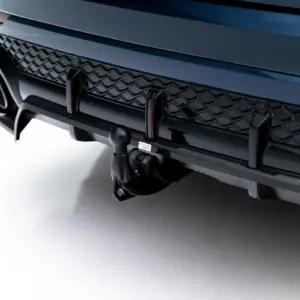 Close-up of a blue car's front bumper showing a honeycomb grille and carbon fiber trim with a towing hitch component visible below.