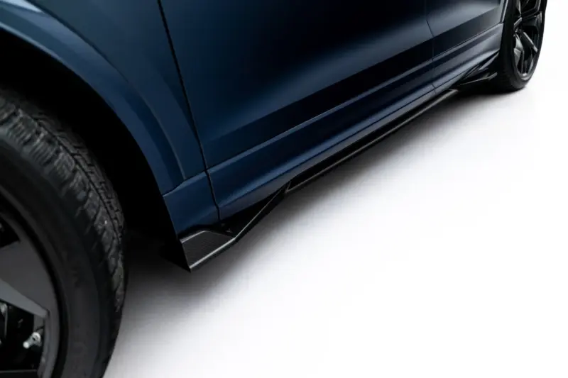 pol_po_Prepreg-Carbon-Fiber-Side-Skirts-Audi-RSQ8-Mk1-Facelift-23817_1webp - OPSHOLDERS Close-up of a dark blue car's lower side panel and wheel, photographed from a low angle against a light background.