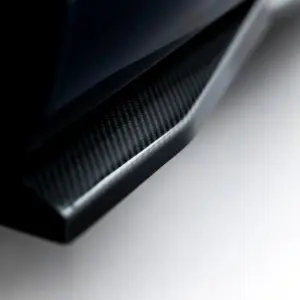 Close-up of a carbon fiber surface along a curved edge, with a dark left side and light gray background.