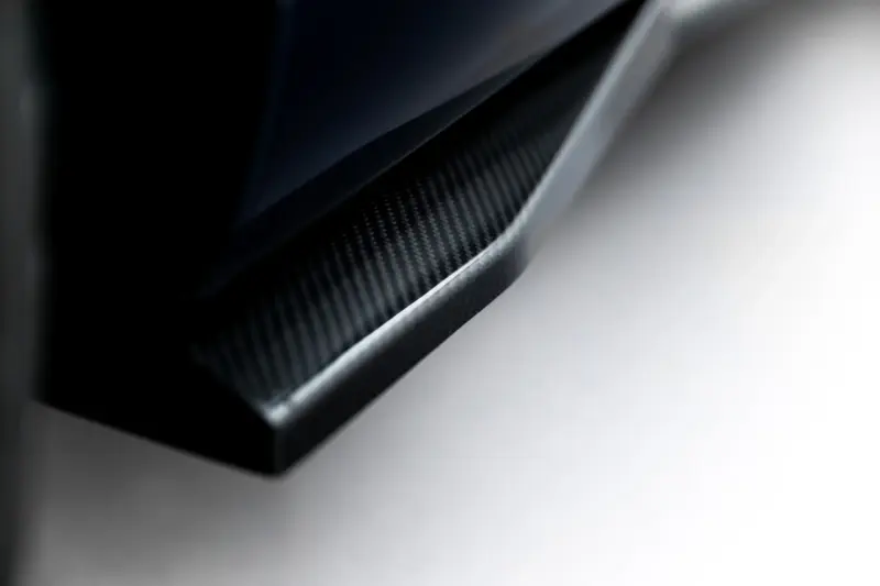 pol_po_Prepreg-Carbon-Fiber-Side-Skirts-Audi-RSQ8-Mk1-Facelift-23817_6webp - OPSHOLDERS Close-up of a carbon fiber surface along a curved edge, with a dark left side and light gray background.