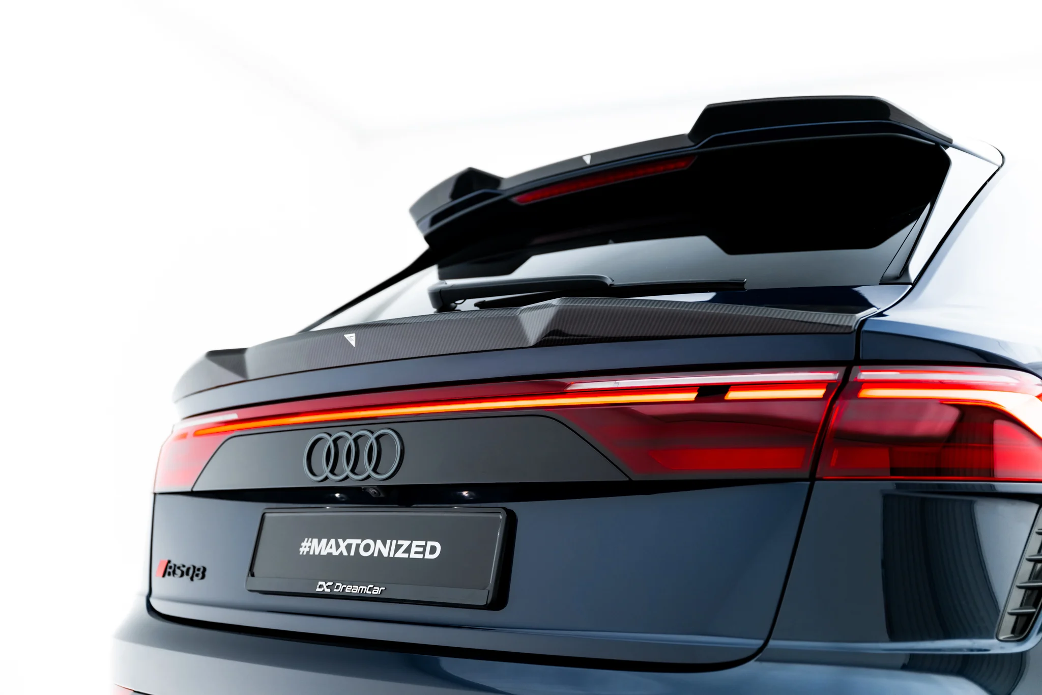 pol_po_Prepreg-Carbon-Fiber-Tailgate-Spoiler-Lower-Audi-RSQ8-Mk1-Facelift-23813_6webp - OPSHOLDERS Rear view of a dark Audi SUV showing the tailgate, spoiler, and red LED taillights with '#MAXTONIZED' on the license area for branding.