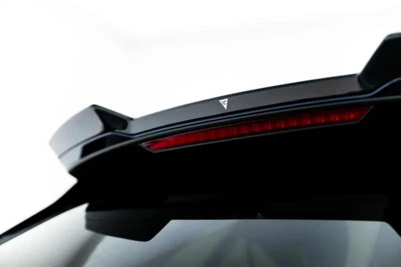Close-up of a car's carbon-fiber rear spoiler with a slim red taillight strip and a small triangular logo in the center area.