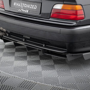 Rear view of a dark car showing dual exhaust pipes and red/amber taillights on a textured floor, with a plate reading #MAXTONIZED.
