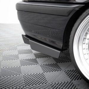 Close-up of a black car bumper and chrome wheel on a textured showroom floor.