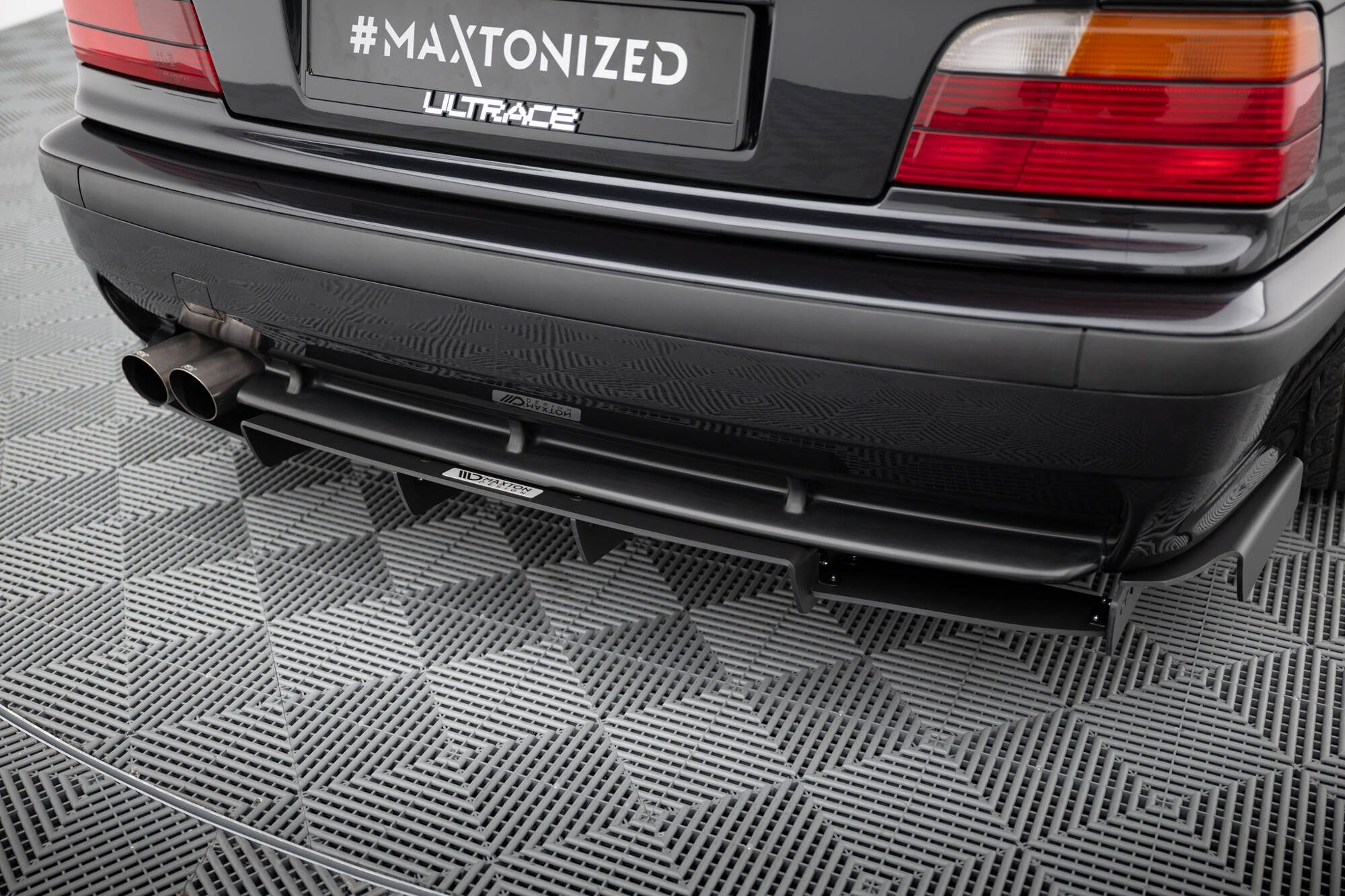 pol_po_REAR-DIFFUSER-BMW-M3-3-M-Pack-Coupe-Cabrio-E36-1829_2jpg - OPSHOLDERS Rear view of a dark car showing dual exhaust pipes and a license plate that reads '#MAXTONIZED' with 'ULTRACE' branding below.