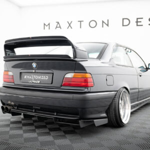 Gray BMW with a large aftermarket rear wing on a showroom floor, displaying the #MAXTONIZED plate.