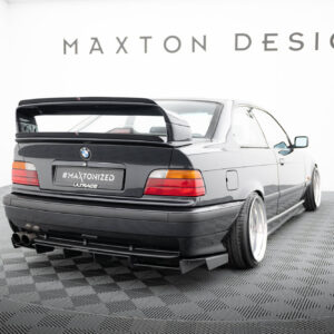 Rear view of a black BMW with a large aftermarket rear spoiler, wide tires, and a '#MAXTONIZED' plate in a studio with 'MAXTON DESIGN' signage above.