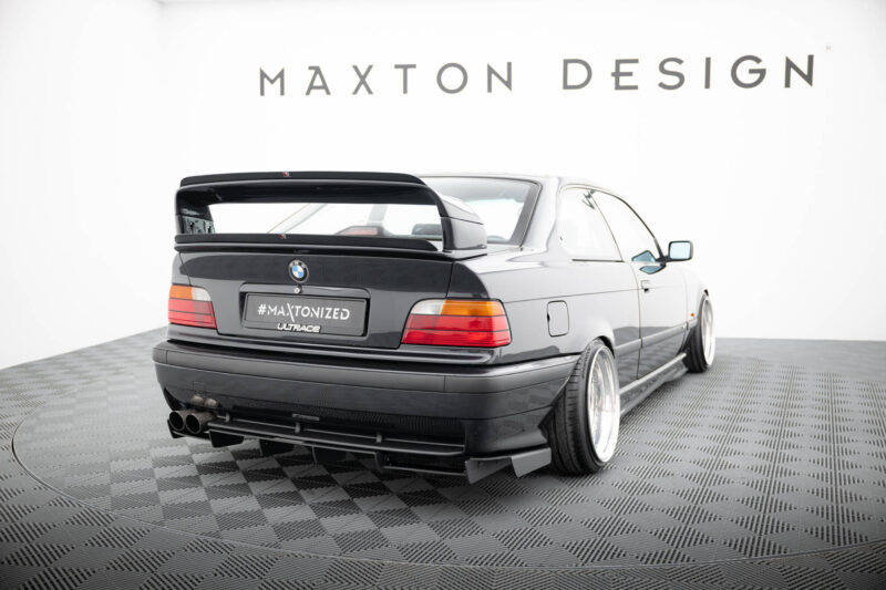 pol_po_REAR-DIFFUSER-BMW-M3-3-M-Pack-Coupe-Cabrio-E36-1829_5jpg - OPSHOLDERS Rear view of a black BMW with a large aftermarket rear spoiler, wide tires, and a '#MAXTONIZED' plate in a studio with 'MAXTON DESIGN' signage above.