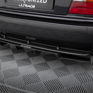 Back of a dark car showing dual exhaust pipes and a shiny bumper on a textured metal floor over a checkered surface