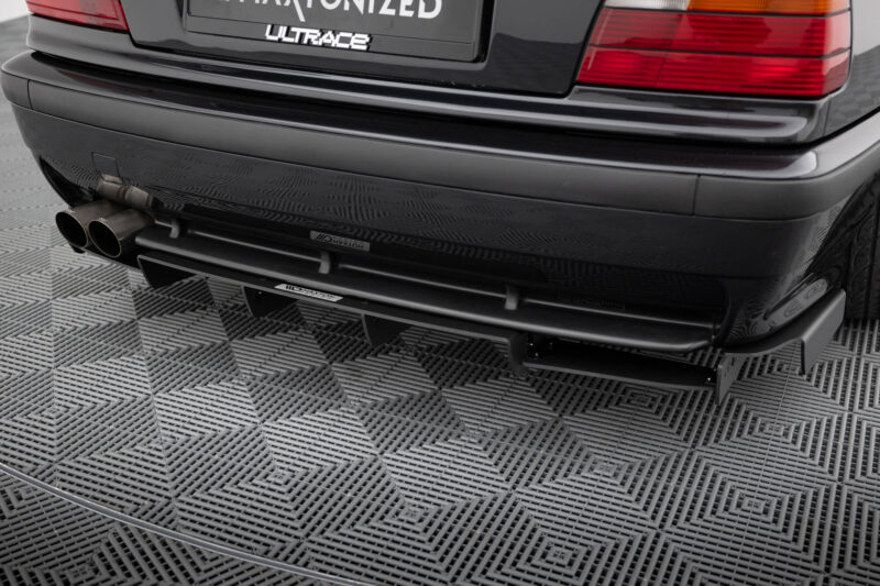 pol_po_REAR-DIFFUSER-BMW-M3-3-M-Pack-Coupe-Cabrio-E36-1829_6jpg - OPSHOLDERS Back of a dark car showing dual exhaust pipes and a shiny bumper on a textured metal floor over a checkered surface