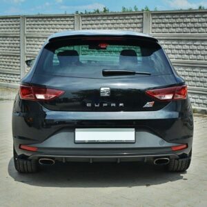 Rear view of a black Seat Cupra hatchback parked on a paved surface with a tall concrete panel fence in the background.