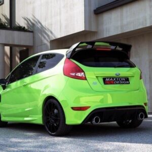 Lime-green hatchback car with a black spoiler parked in front of a modern beige building, rear three-quarters view showing dual exhausts and black wheels.