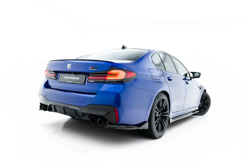 Blue BMW sedan shown from a rear three-quarter angle, featuring M Competition badge and a sporty rear diffuser.