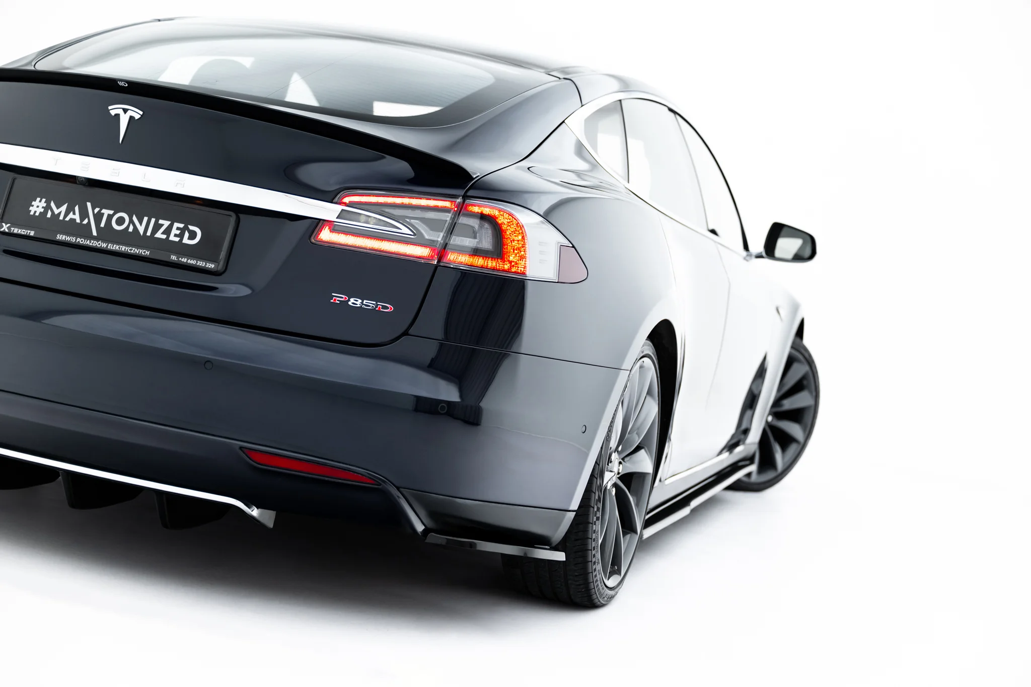 pol_po_Rear-Side-Splitters-V-2-Tesla-Model-S-Mk1-23945_4webp - OPSHOLDERS Rear three-quarter view of a dark gray Tesla with a '#MAXTONIZED' plate and P85D badge on the trunk area.