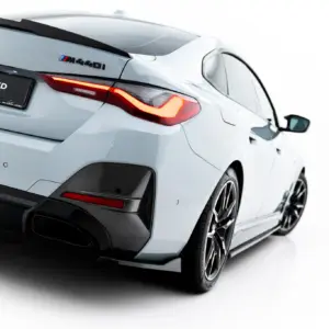 Rear three-quarter view of a white BMW sport coupe with carbon fiber rear diffuser and illuminated taillights in a studio setting