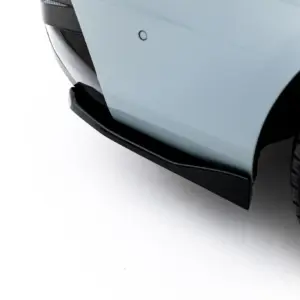 Close-up of the front left corner of a light blue car, showing part of the bumper, front splitter, and wheel with tire tread on a white backdrop.