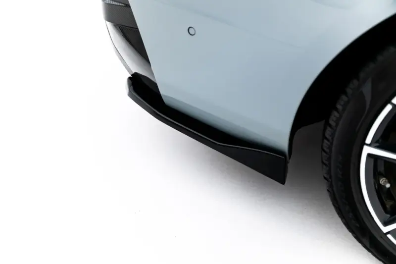 Close-up of the front left corner of a light blue car, showing part of the bumper, front splitter, and wheel with tire tread on a white backdrop.