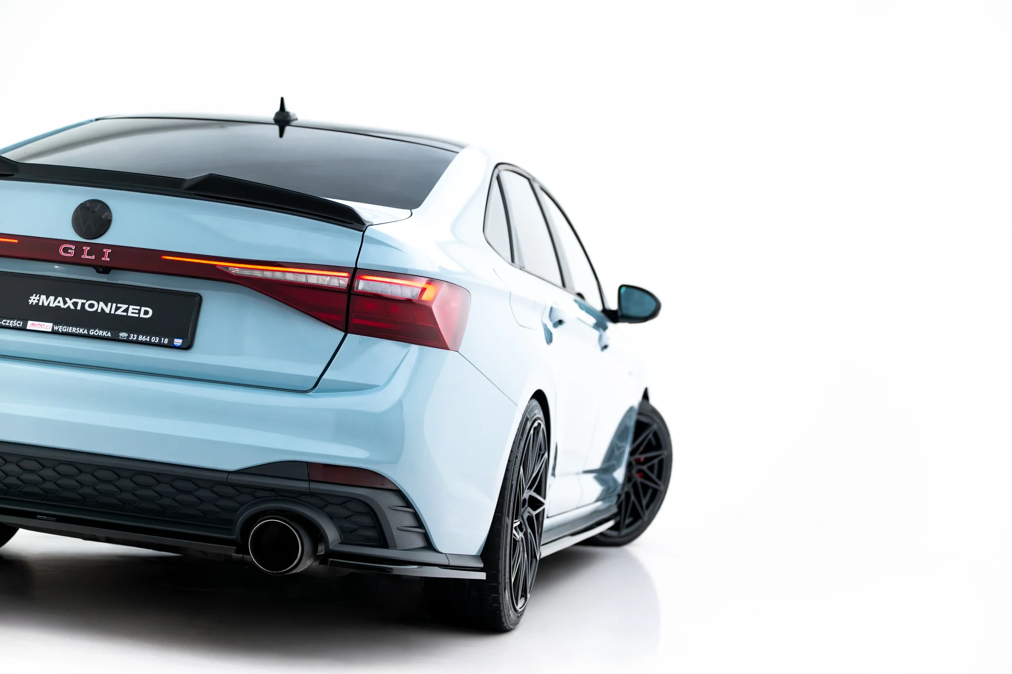 pol_po_Rear-Side-Splitters-Volkswagen-Jetta-GLI-Mk7-Facelift-2-23932_3webp - OPSHOLDERS Rear three-quarter view of a light-blue VW GLI with a red taillight bar and sporty rear bumper on a white background