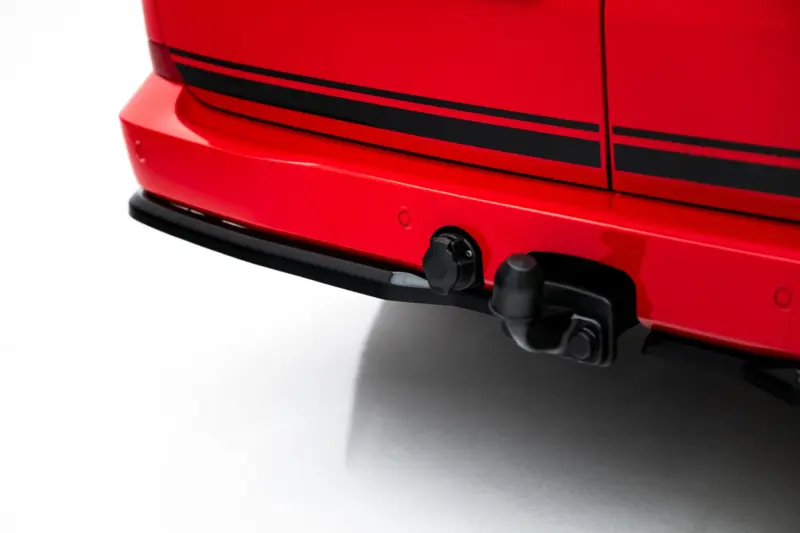 pol_po_Rear-Side-Splitters-Volkswagen-Transporter-T7-23936_2webp - OPSHOLDERS Close-up of a red car bumper showing a black tow hitch and trim lines along the side panel