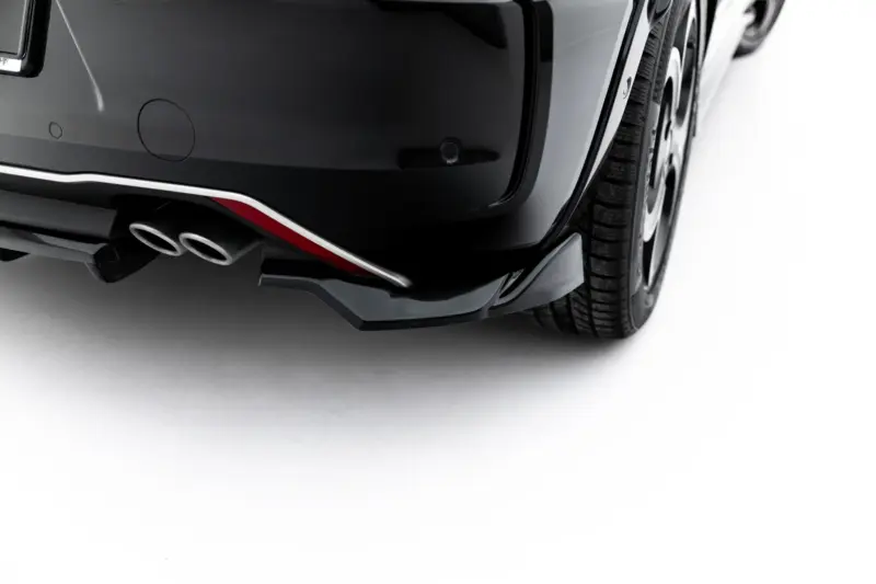 Close-up of a dark car's rear bumper with dual exhaust tips and part of the rear wheel visible.