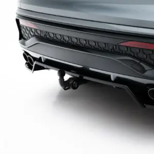 Close-up of the rear end of a sleek dark SUV showing taillight, bumper, and dual exhaust tips on a white surface backdrop.