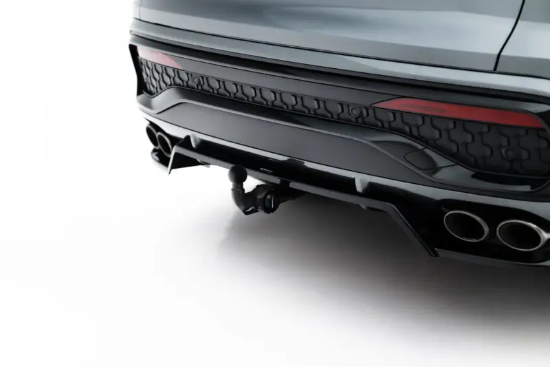 Close-up of the rear end of a sleek dark SUV showing taillight, bumper, and dual exhaust tips on a white surface backdrop.