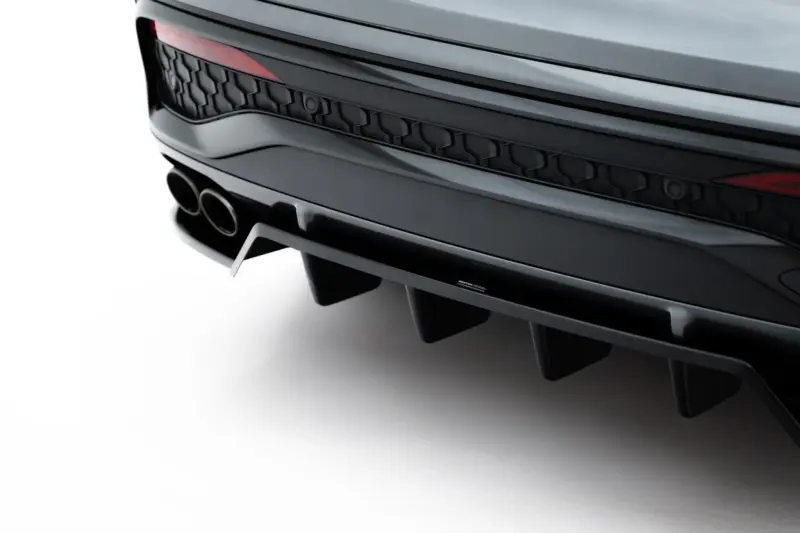 Close-up of a sleek car rear showing dual exhaust outlets, dark honeycomb rear grille, and a red taillight edge on the left edge of the image.