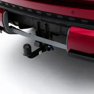 Close-up of a red car's rear bumper with a trailer hitch and tow ball assembly visible beneath the bumper.