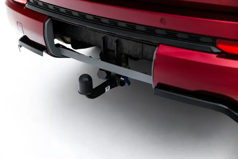 pol_po_Rear-Splitter-with-vertical-bars-Jeep-Grand-Cherokee-L-Mk5-23903_2webp - OPSHOLDERS Close-up of a red car's rear bumper with a trailer hitch and tow ball assembly visible beneath the bumper.