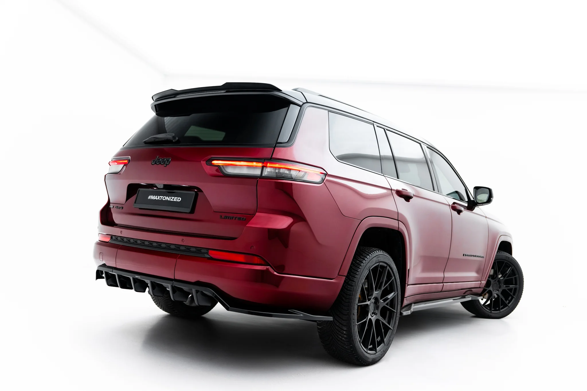 pol_po_Rear-Splitter-with-vertical-bars-Jeep-Grand-Cherokee-L-Mk5-23903_6webp - OPSHOLDERS Red Jeep SUV viewed from the rear-right at a three-quarter angle, showing taillights, spoiler, and large dark wheels.