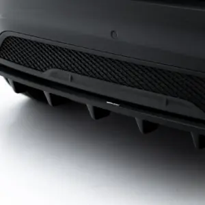 Close-up of a dark car bumper with a mesh grille and a Maxton Design badge on the lower lip on the front fascia.