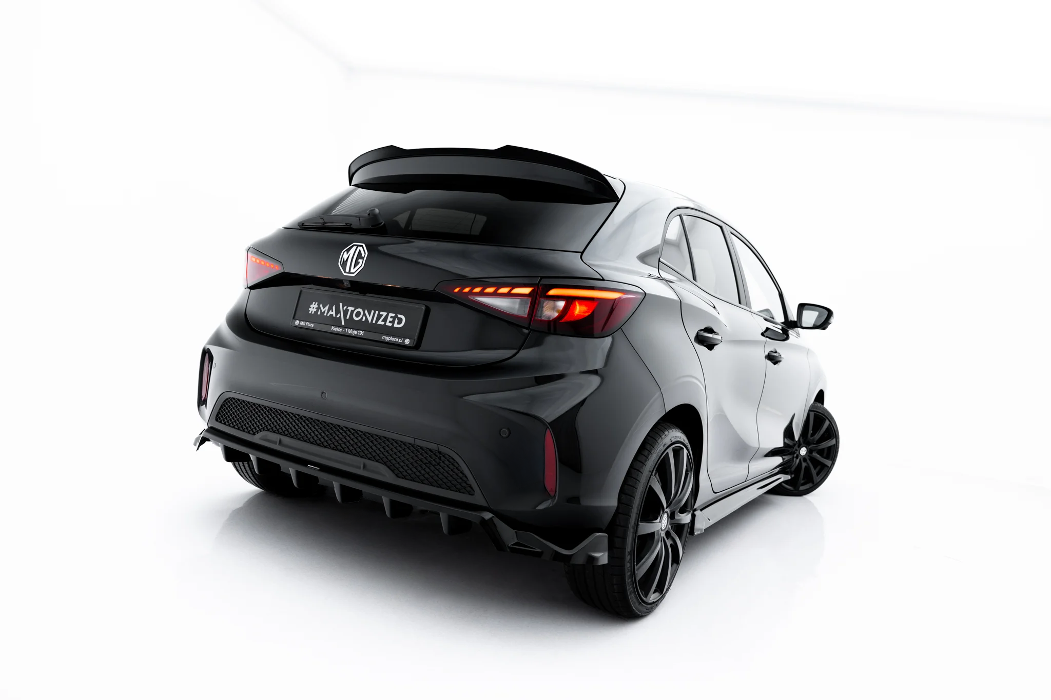 pol_po_Rear-Splitter-with-vertical-bars-MG-3-Mk1-23918_3webp - OPSHOLDERS Rear view of a dark gray MG hatchback with a sporty spoiler and illuminated taillights on a white studio backdrop