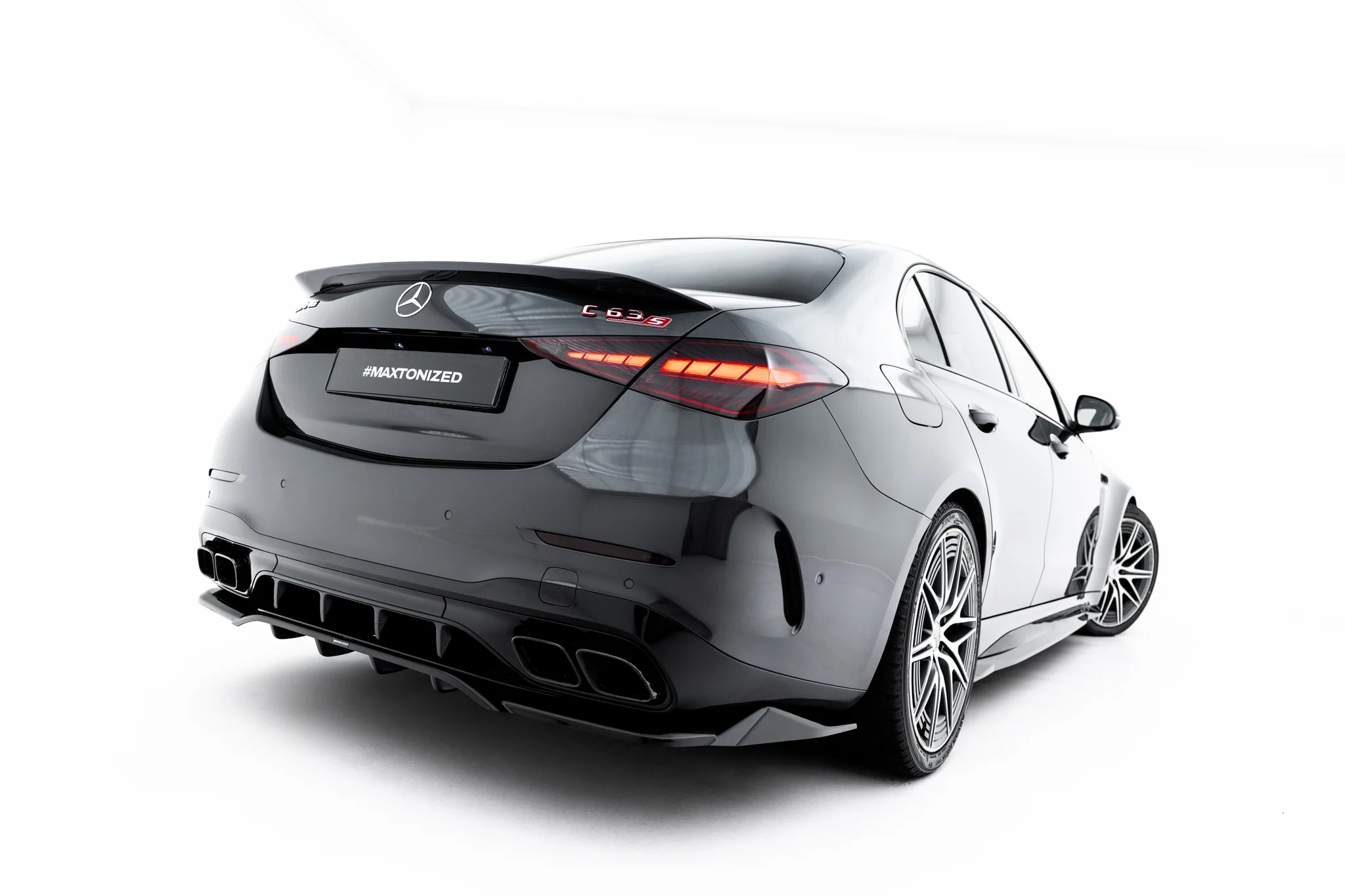 pol_po_Rear-Splitter-with-vertical-bars-Mercedes-AMG-C63-Sedan-Estate-W206-S206-23826_4webp - OPSHOLDERS Rear three-quarter view of a dark gray Mercedes-Benz C63 S with a #MAXTONIZED plate on the trunk lid and prominent taillights.