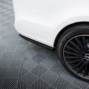 Close-up of a white car’s front fender and black alloy wheel on a checkered gray floor.