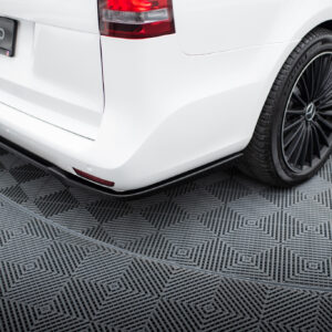 Rear view of a white car showing the tail light, curved bumper, and a tow hitch on a patterned floor surface.